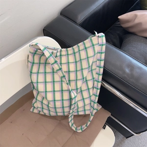 Detail of green and purple plaid canvas bag with simple wish label on a white chair