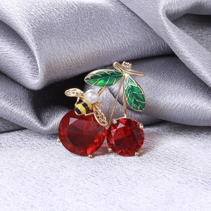 Macro shot of cherry and bee brooch with red stones and pearls on grey silk fabric