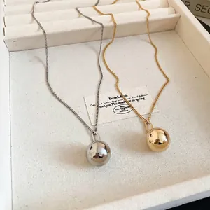 Polished gold and silver ball pendant necklaces on a white textured jewelry tray