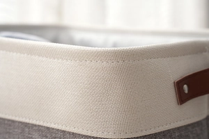 Close-up of gray cotton linen storage bin with brown leather handles and reinforced stitching