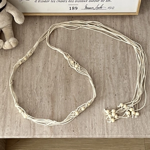 Detail of bohemian cream woven cotton belt with light wood beads on stone background