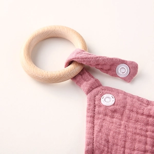Detail of pink cotton baby comforter with smooth wooden ring and textured muslin fabric