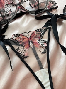 Close-up of intricate butterfly embroidery on black mesh lingerie with satin ribbon ties