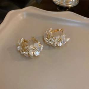 Detailed close-up of golden C-shaped hoop earrings with white 3D flowers and crystals
