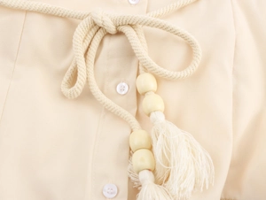 Detail eines beigen Hemdkleides mit geflochtenem Kordelgürtel, Holzperlen und Quasten