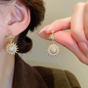 Detail of gold solar planet earrings with white zircon stones on model ear