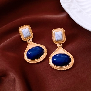 Detailed close-up of vintage gold earrings with marble inlay and blue oval gemstones