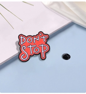 Close-up of DON'T STOP metal enamel pin with red background and black rubber clutch