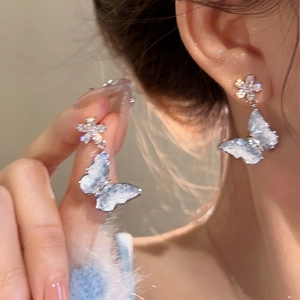 Close-up of delicate blue butterfly earrings with shimmering crystal floral studs.
