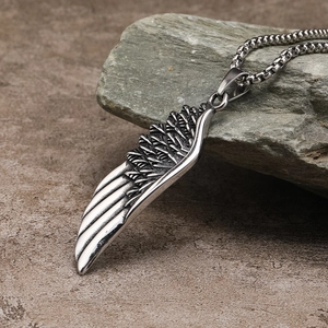 Macro detail of a silver stainless steel feather wing pendant on a grey rock surface