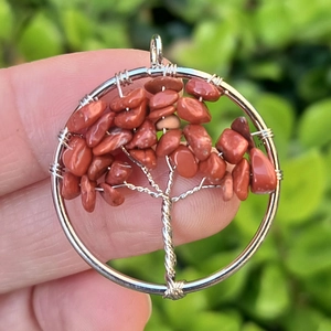 Macro view of red gemstone Tree of Life pendant held by hand against green foliage