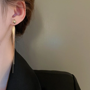 Detail showing elegant gold tassel earrings with sleek snake chains on a female model