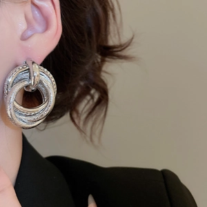 Macro detail of silver multi-layered circular earrings worn on a model in a black suit