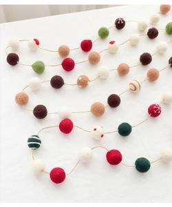 Handmade wool felt ball garland with festive snowflake patterns on white linen fabric