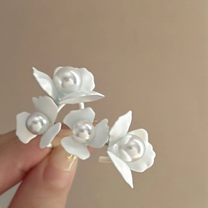 Macro detail of white floral earrings with pearls and matte finish held by hand
