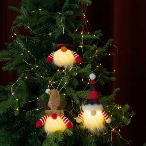 Three glowing Christmas gnomes hanging on a lit Christmas tree with plush LED ornaments