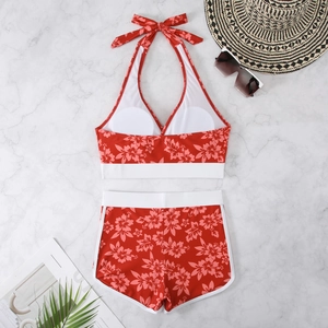 Flat lay of red floral halter bikini set with white trim, sun hat, and summer beach props