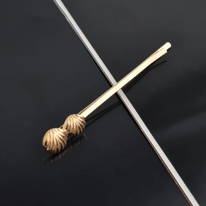 Close-up of golden metal hair clip featuring textured shell ornaments on a dark surface