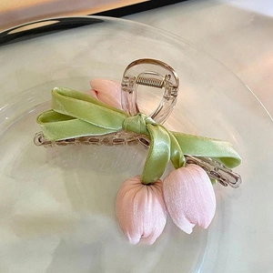 Detail of pink fabric tulip and green bow hair claw clip on clear glass tray