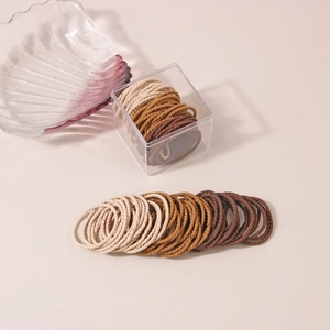 Macro shot of high-elasticity braided hair ties in earthy gradient tones with acrylic box