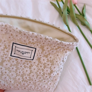 Close-up of white daisy lace embroidery and Time to Party woven label on makeup bag