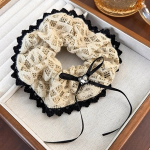 Detail of beige lace hair scrunchie with black trim, ribbon bow, and rhinestone accents