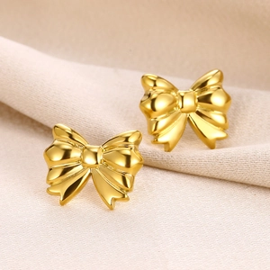 Macro detail of 18K gold-plated bow earrings with high-polish finish on beige fabric