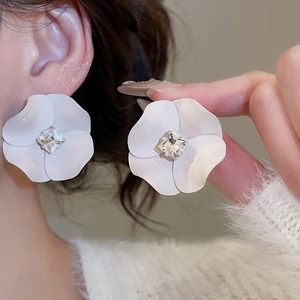 Close-up of white floral stud earring with a central diamond-like crystal on ear