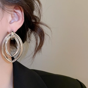 Gros plan de boucles d'oreilles ovales argentées portées avec un blazer noir