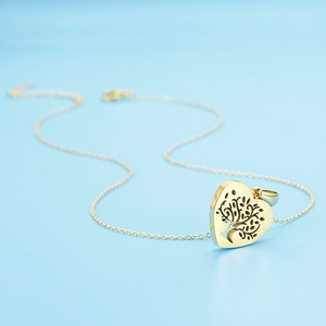Detailed view of a gold heart pendant with a tree of life cutout on a blue background