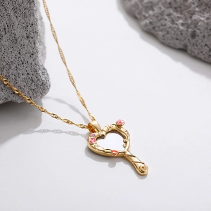 Golden heart mirror pendant necklace with pink enamel details on grey rocks