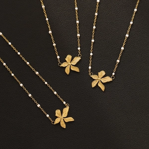 18K gold plated flower necklace with white pearls on a minimalist black textured background