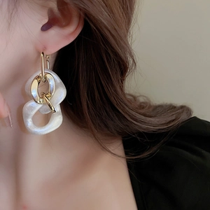 Detail shot of a model wearing large gold chain links with pearl white acrylic hoop earrings