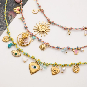 Layered gold necklace with colorful rope, evil eye, sun and moon charms on white background