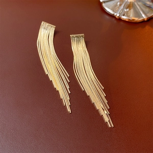 Close-up of golden tassel chain drop earrings on a textured reddish-brown leather surface