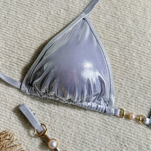 Detail of metallic purple bikini top with pearl chains and gold ring accents on knit fabric