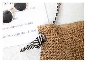 Detail of straw woven bag showing the connection between striped strap and metal ring
