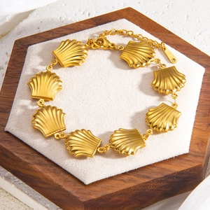 Adjustable 18k gold plated shell link bracelet with cross charm on a wooden display