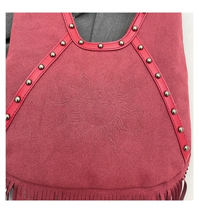 Detail of rose pink suede shoulder bag with metal studs, fringe, and sun totem texture