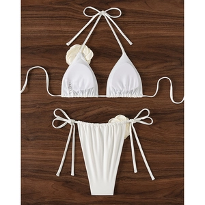 White two-piece bikini with 3D floral accents and side-tie bottoms on wood background