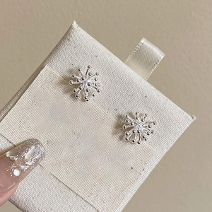 Detail shot of silver fireworks earrings with pearls on a textured beige display