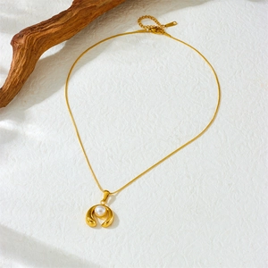 Gold stainless steel U-shaped pearl pendant necklace with thin snake chain on textured background