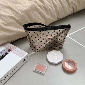 Detail of cream mesh makeup bag with heart print featuring toiletries and a black zipper