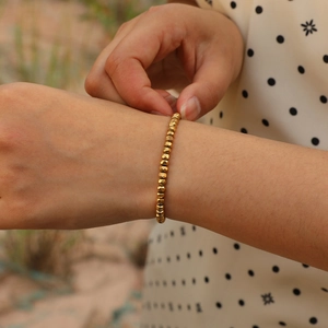Macro shot of gold faceted beaded bracelet on a woman wrist with outdoor background