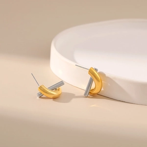 Close-up of gold and silver contrast twist earrings on a white ceramic plate