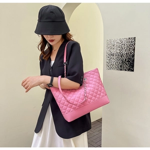 Detail of pink quilted tote bag with chain strap shown by model in modern architectural setting