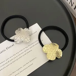 Close-up of gold and silver four-leaf clover hair ties with grid texture on a black tray