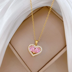 Macro detail of gold heart necklace with pink crystals on white silk background