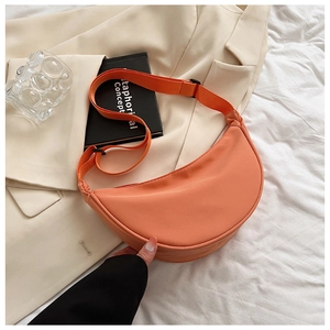 Detail view of an orange nylon half-moon crossbody bag placed on a beige blazer