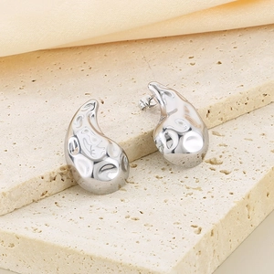 Close-up of silver drop earrings with lava texture on a travertine stone stand
